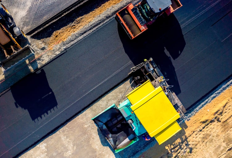 Luftaufnahme mehrerer Baumaschinen beim Verkehrswegebau mit Asphalt.