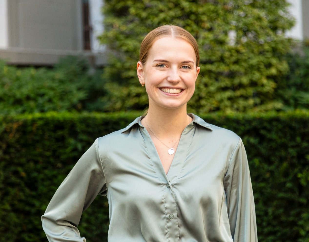 Portraitaufnahme einer BAG Mitarbeiterin vor einer Hecke.