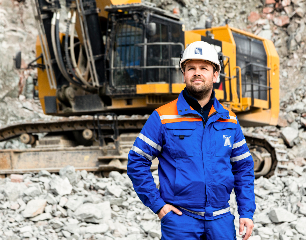 Mitarbeiter im Steinbruch bei der Produktion mit einer Baumaschine im Hintergrund.